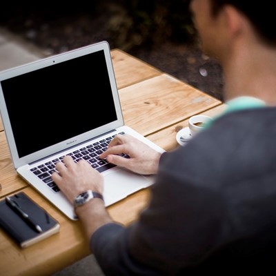A man using a laptop while sitting at a picnic table outside.
