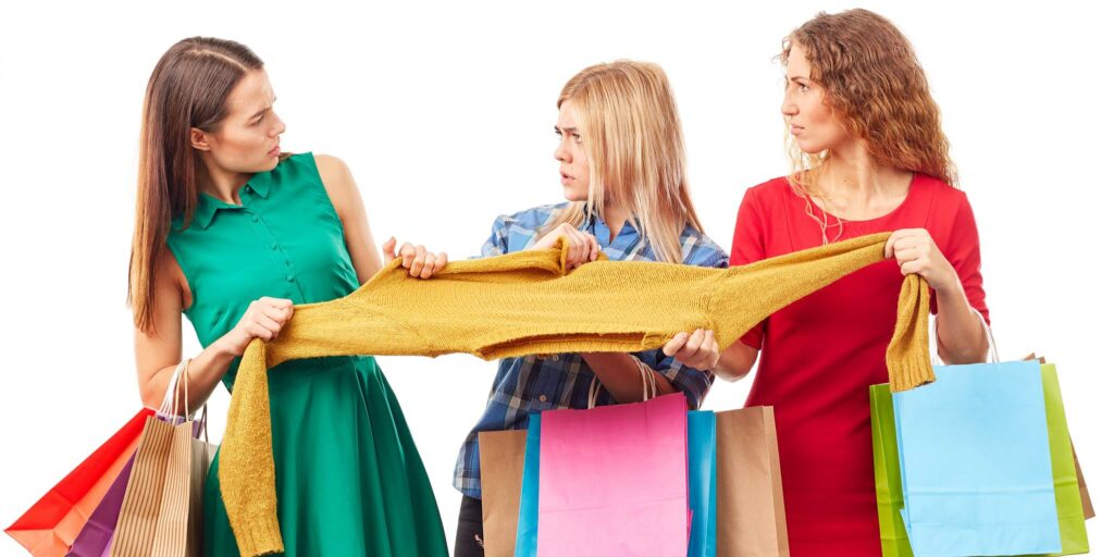 Three women with shopping bags all grabbing onto the same sweater.