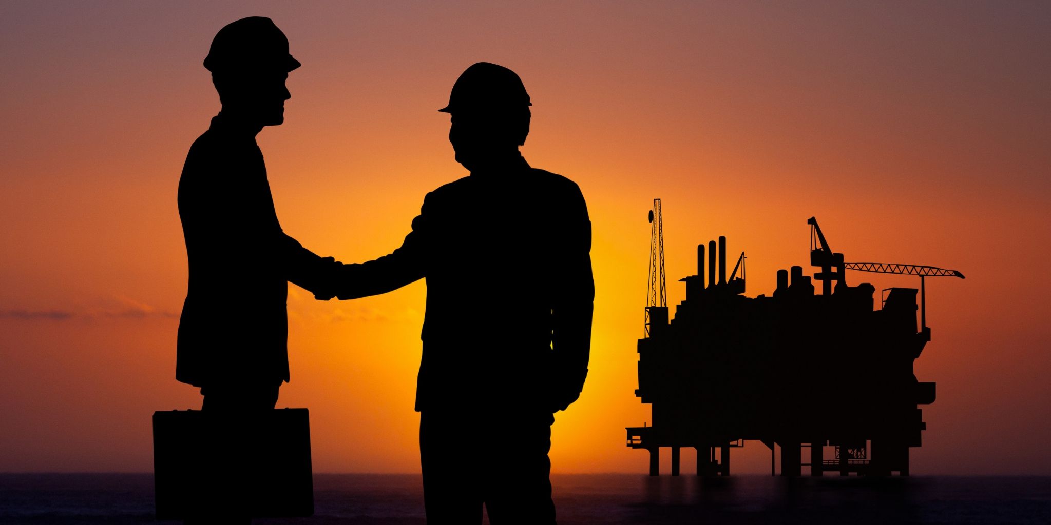 Two men shaking hands at sunset with an offshore oil rig in the background.